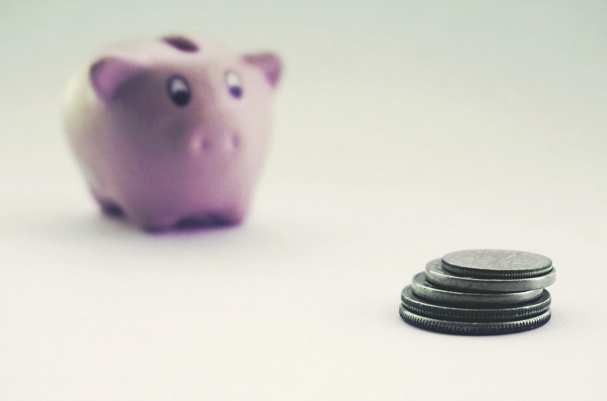 A small stack of coins next to a pink piggy bank on a plain background