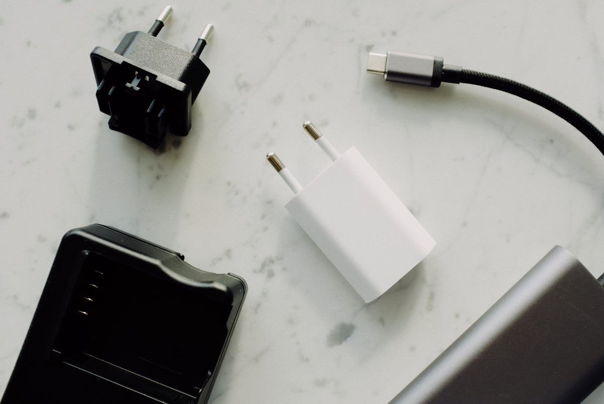 A Type-C charging cable, wall adapters, and a battery charger laid out on a marble surface