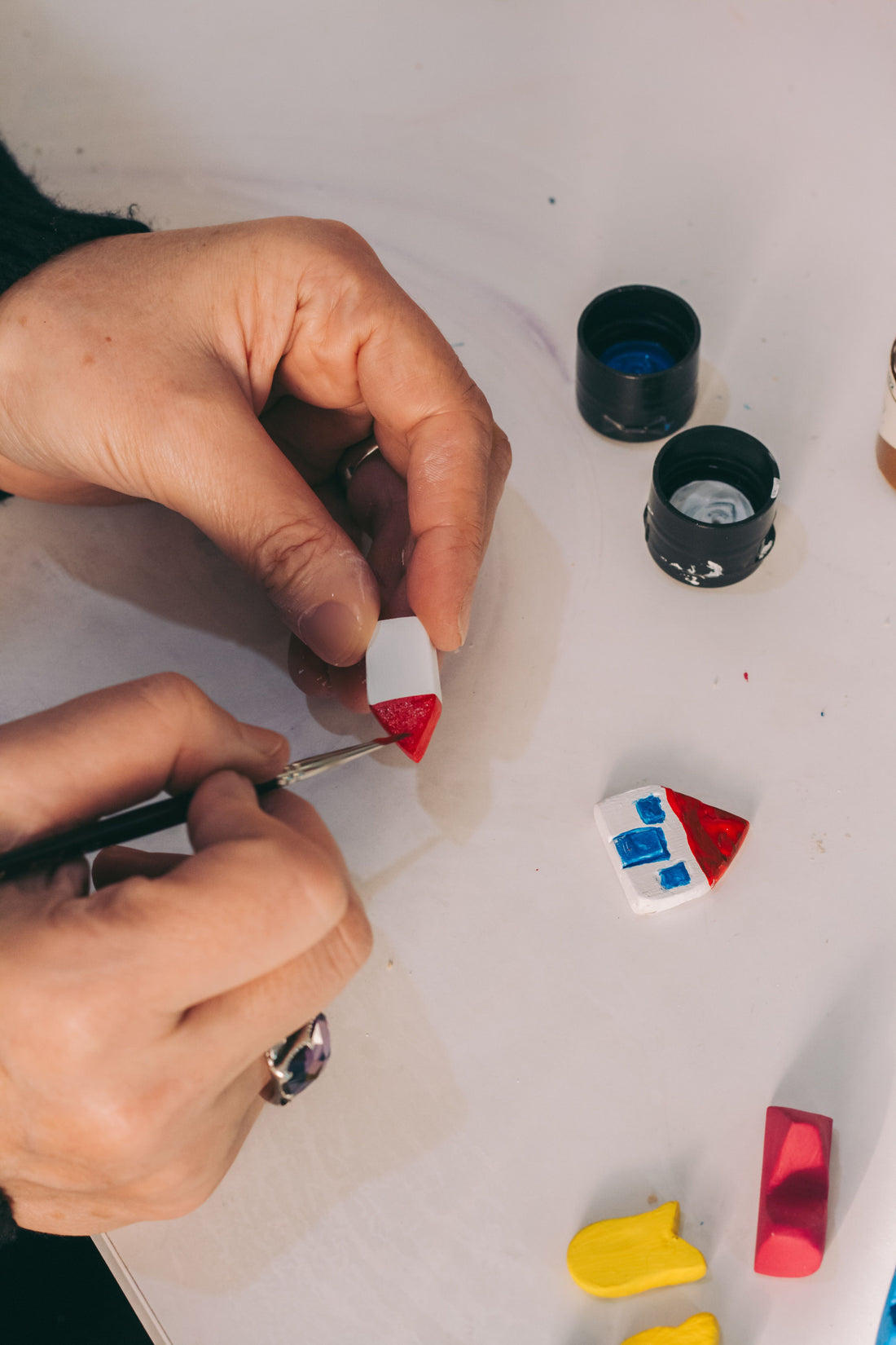 Close-up of a hand using a fine-tip brush to paint a small clay figurine in red, white, and blue
