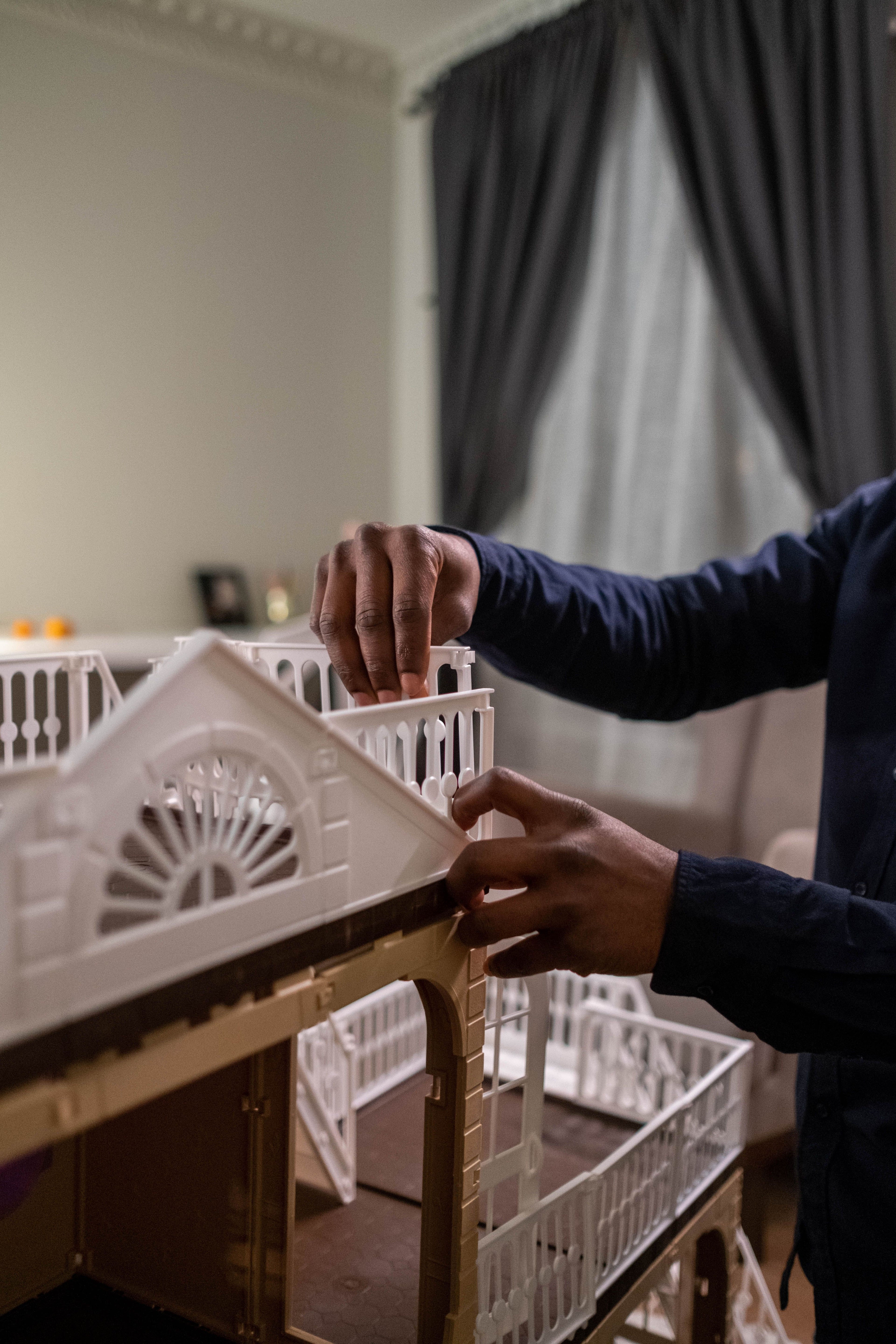 Hands carefully assembling a miniature house kit, piece by piece