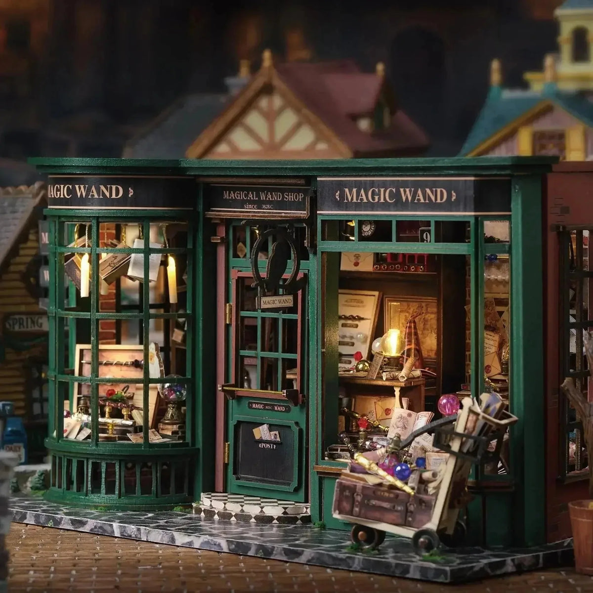 Magical Wand Shop miniature wizard shop with a lit bay window, green door and luggage trolley