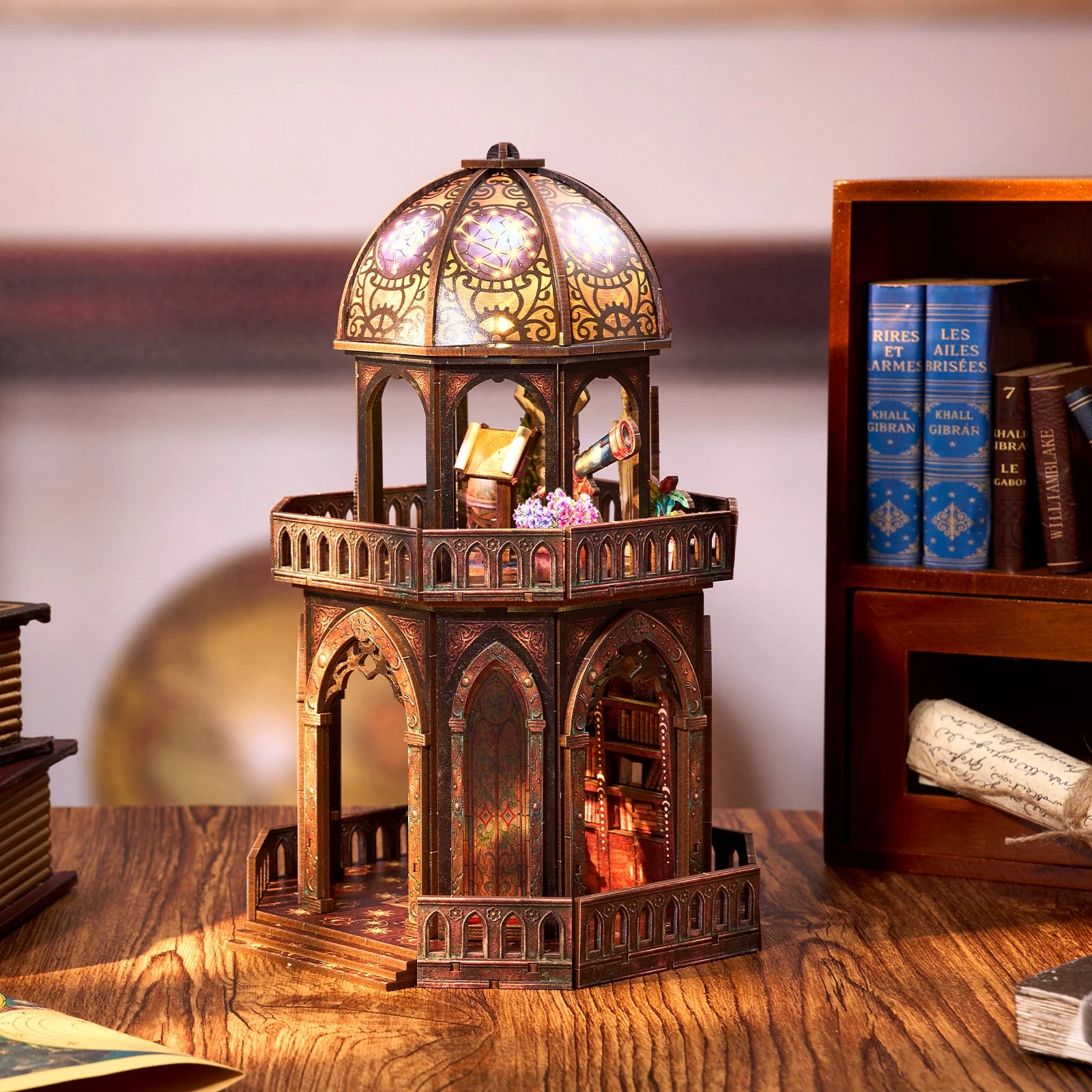 Assembled observatory dollhouse kit displayed on a shelf between books, dome lit with warm LED light